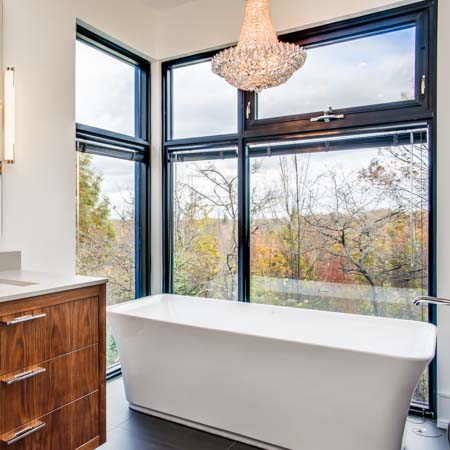 view of a freestanding tub beside tall windows with views of trees