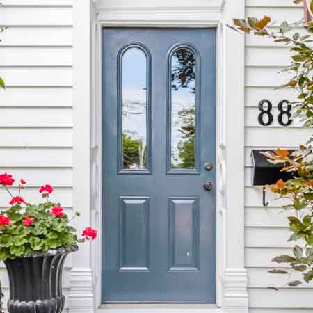 closeup on a front door with white siding and a dark blue door